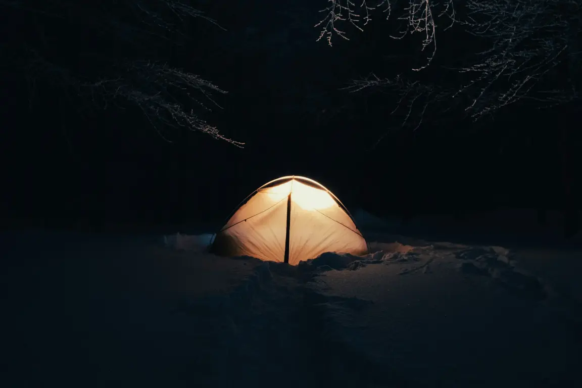 夜の雪原で明かりの灯るテント