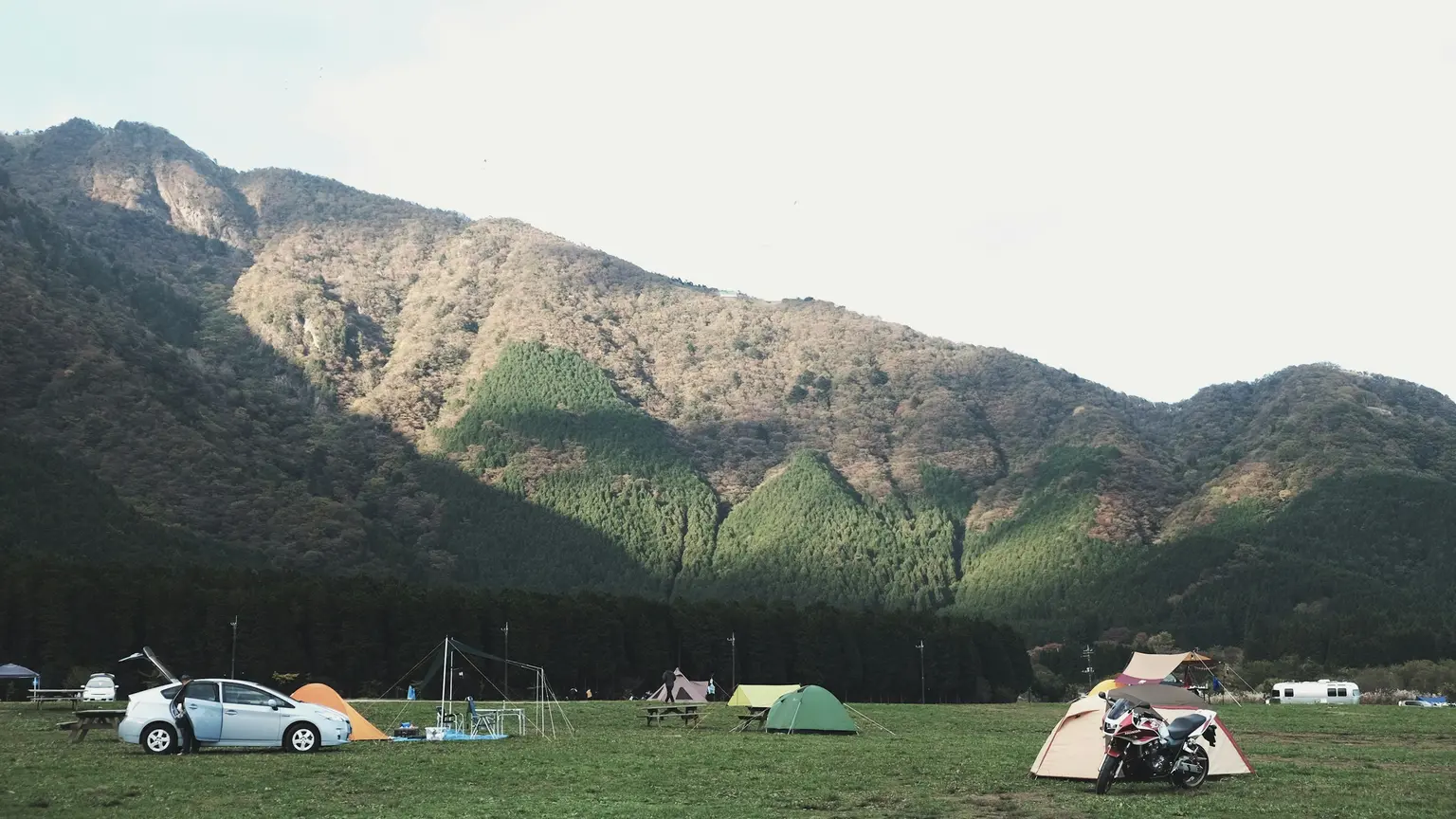 山並みを背にした広い草地のキャンプ場に、色とりどりのテントと車、バイクが点在している