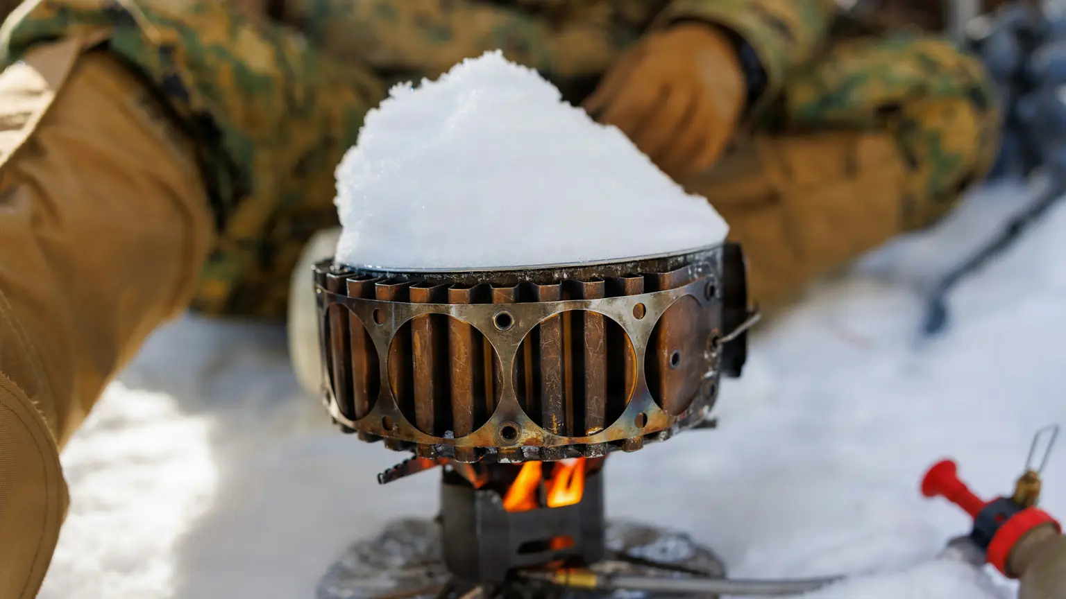 雪の上に置いたシングルバーナーの炎で、鍋の雪を溶かしている